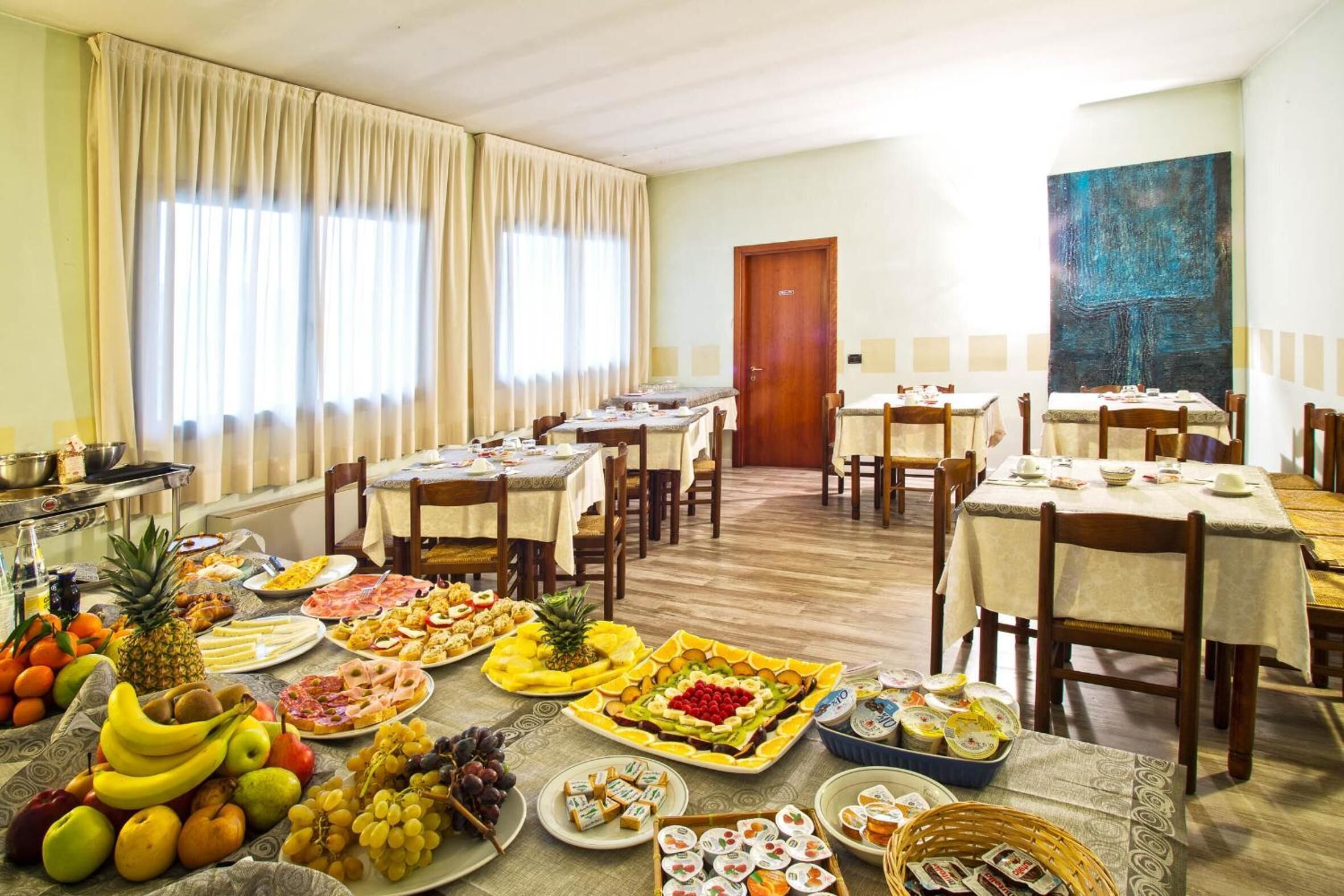 Zona pranzo con diversi tavoli apparecchiati per la colazione, con una varietà di frutta, pasticcini e bevande.