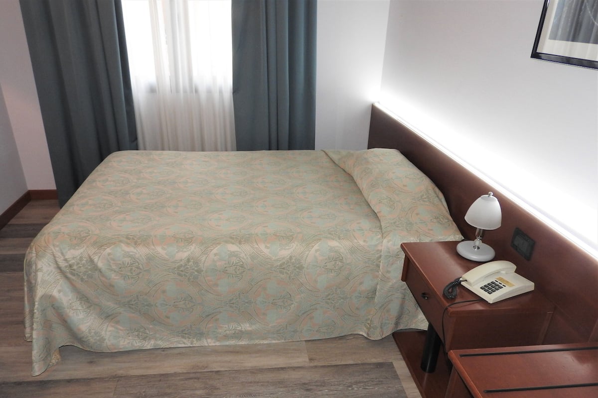Una habitación de hotel con cama, una mesita de noche de madera, una lámpara y un teléfono.
