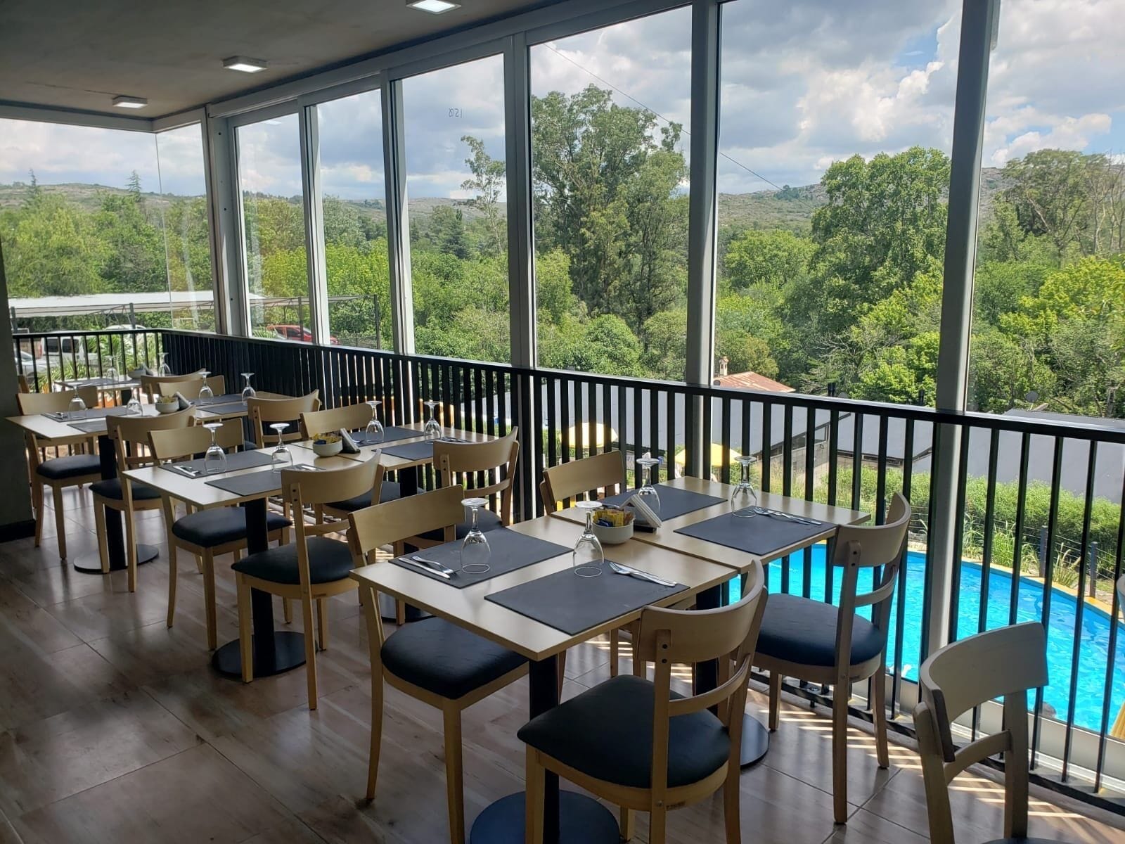 Restaurante com área externa, vista para uma piscina e paisagem com colinas e árvores.