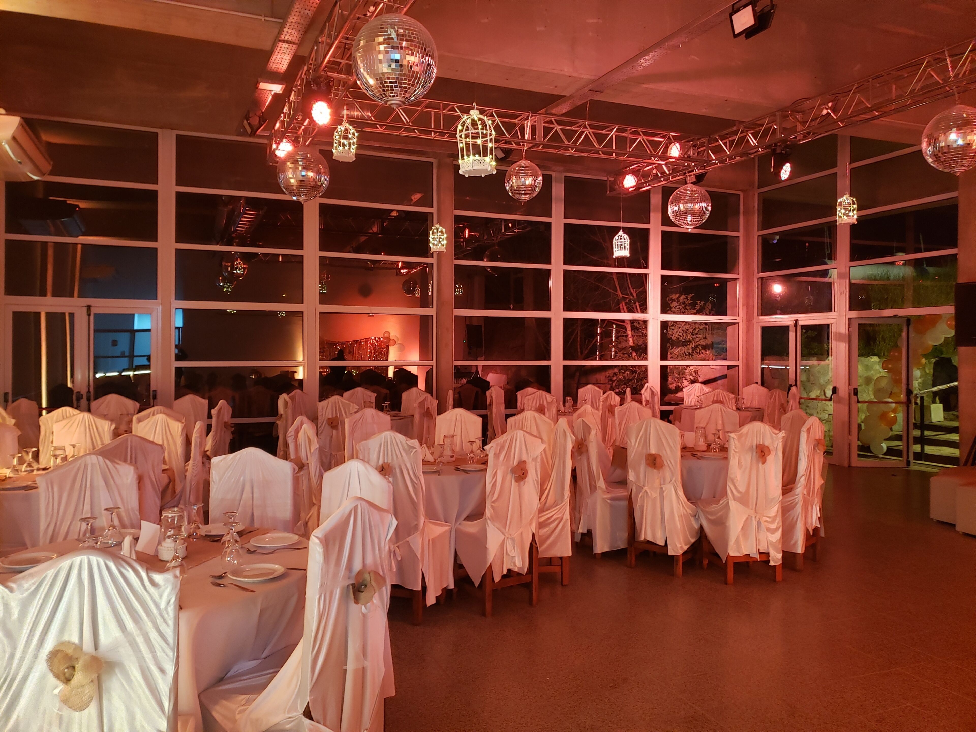 Un salón de banquetes con mesas cubiertas con manteles blancos y sillas adornadas con telas blancas.