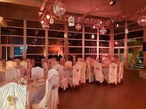 A banquet hall with tables covered in white tablecloths and chairs draped with white cloths.