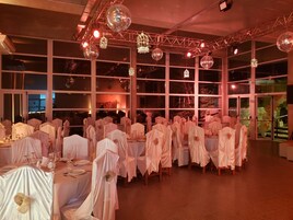 Un salón de banquetes con mesas cubiertas con manteles blancos y sillas adornadas con telas blancas.