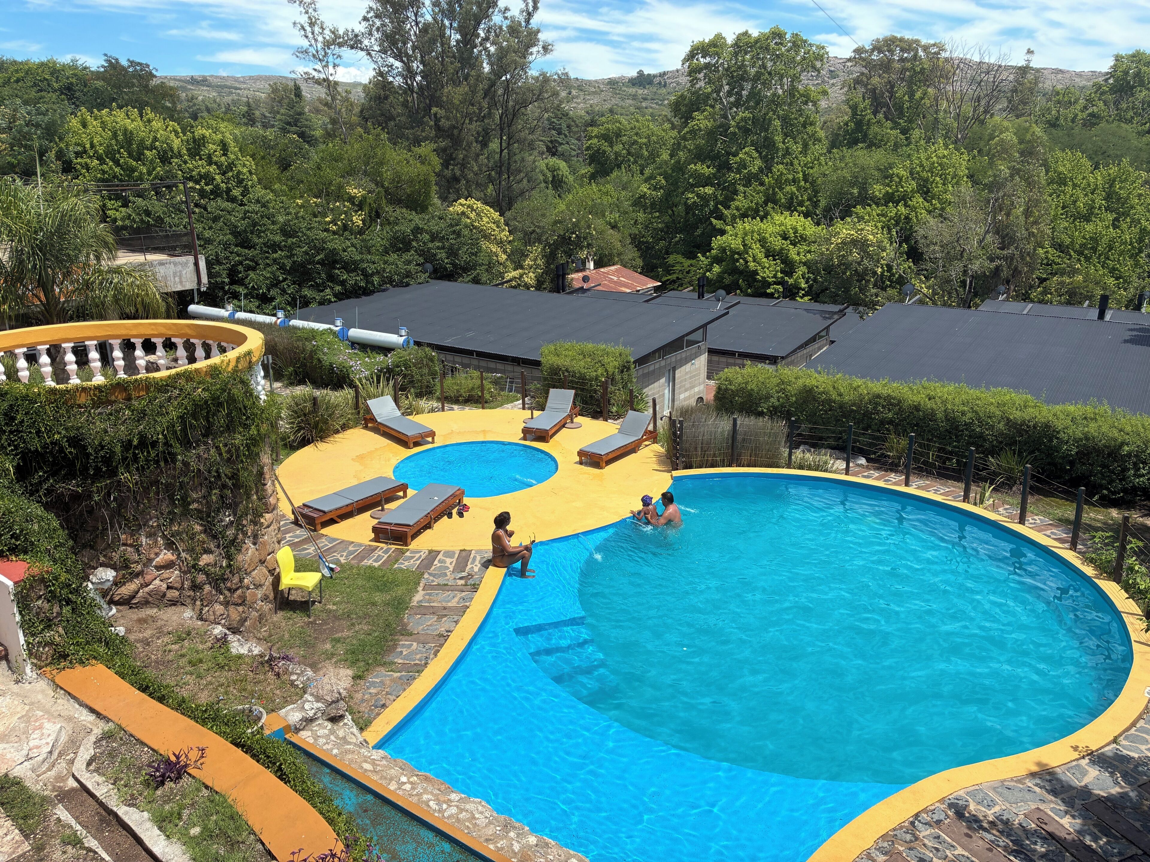 Una piscina de borde curvo, rodeada de sillones de descanso y una terraza amarilla.