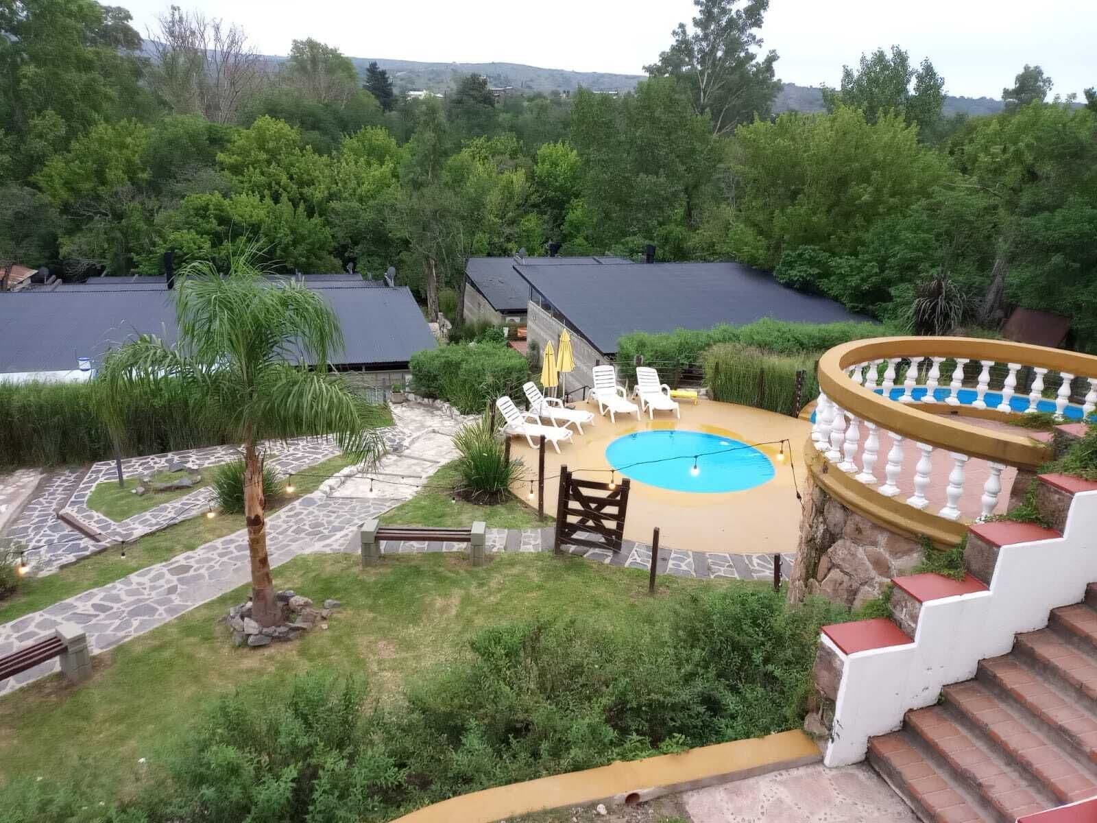 Un área de piscina con sillones de descanso, una piscina pequeña y una escalera que lleva a una terraza cubierta.