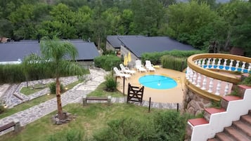 Un área de piscina con sillones de descanso, una piscina pequeña y una escalera que lleva a una terraza cubierta.
