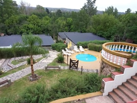 Un área de piscina con sillones de descanso, una piscina pequeña y una escalera que lleva a una terraza cubierta.