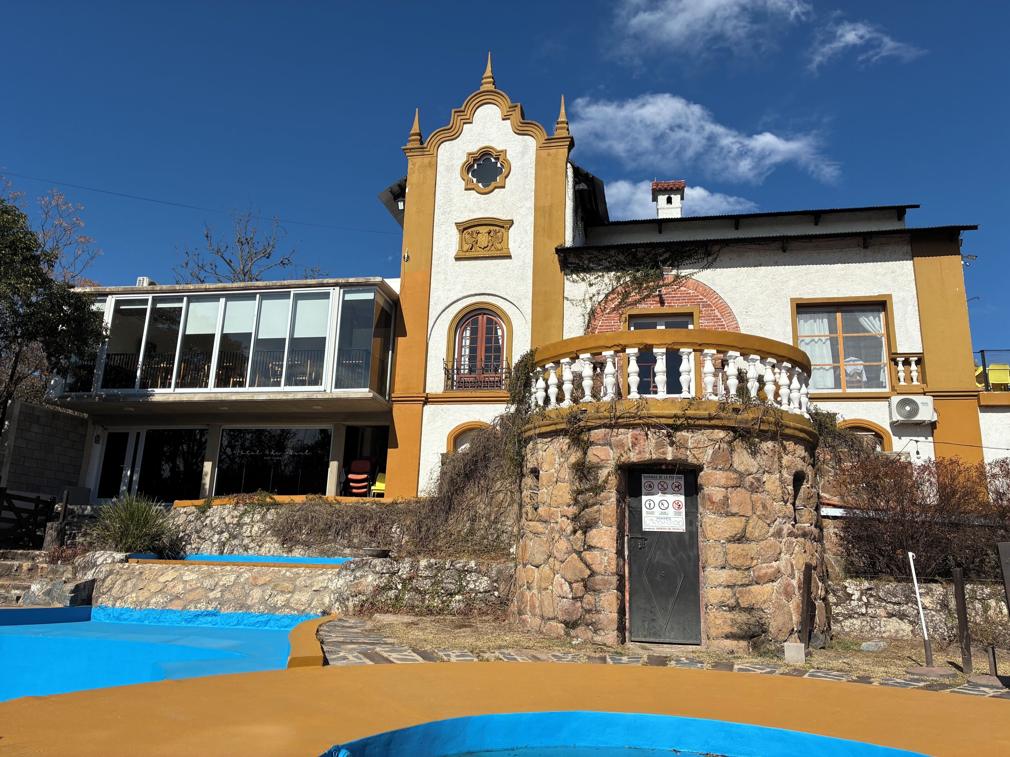 Un edificio con torre, piscina y muro de piedra.