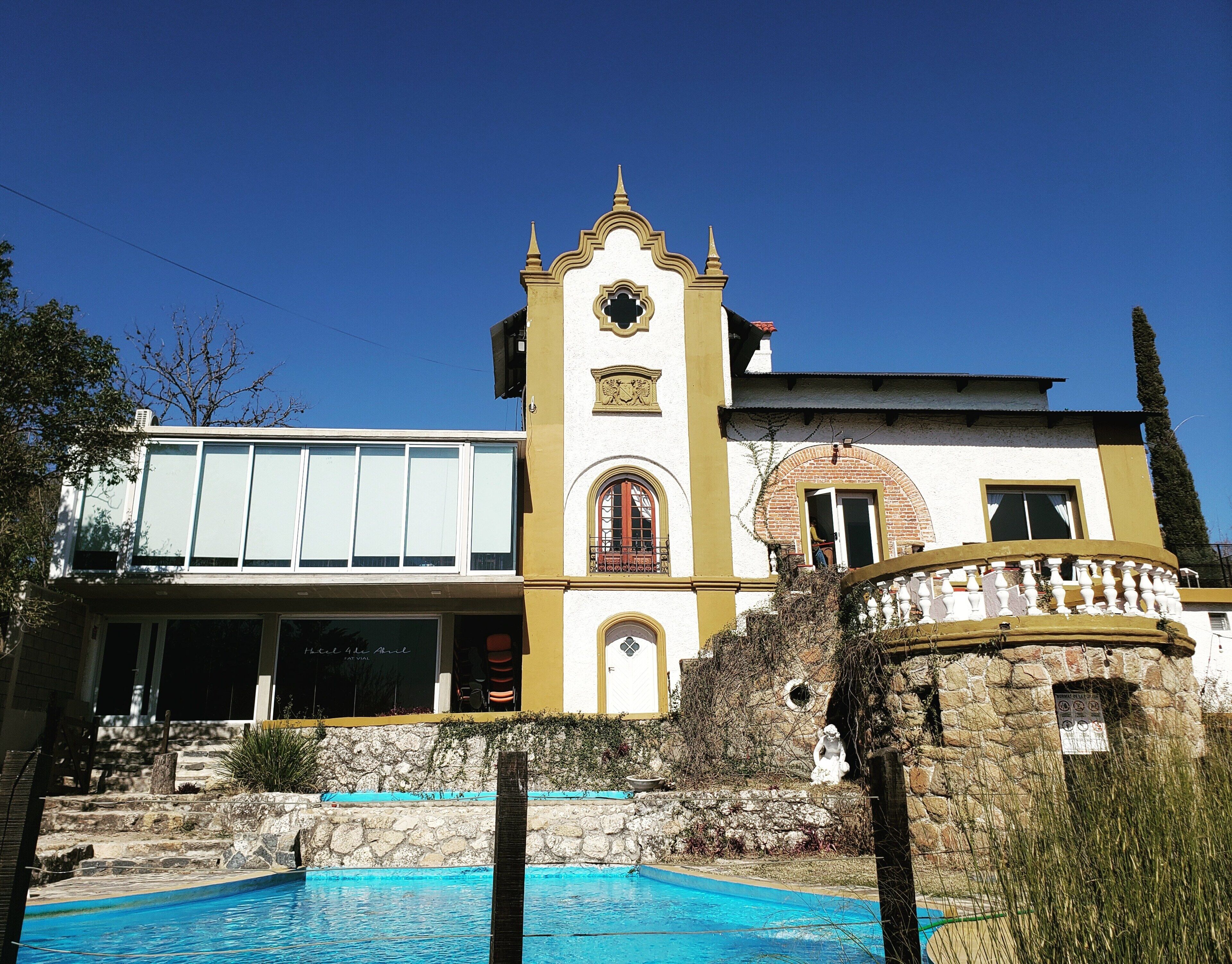 Un hotel con piscina, una torre de campanas y una amplia entrada con ventanas.