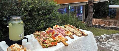 A buffet table with various food items and a beverage dispenser, set outdoors with a hotel sign in the background.