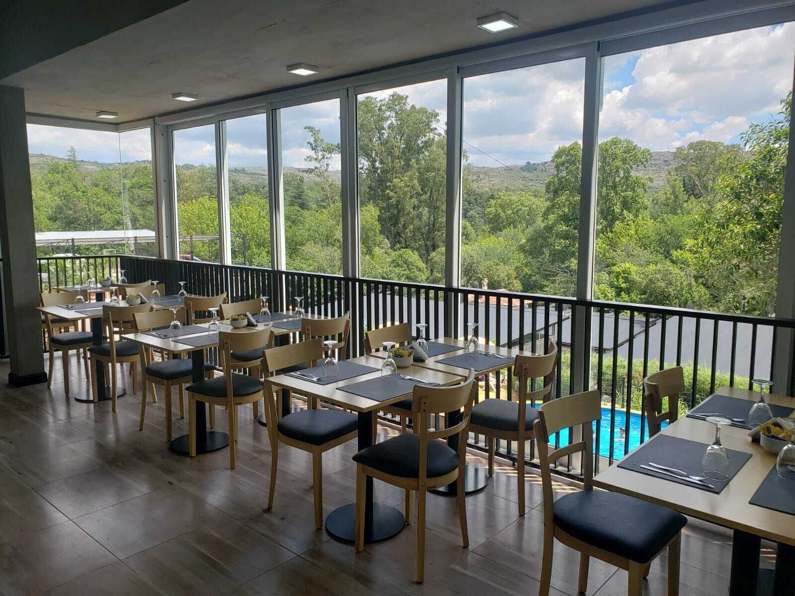 Comedor con mesas y sillas, amplias ventanas con vistas a zonas verdes y colinas.