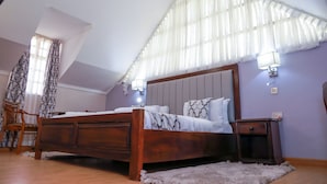 A bedroom with a wooden bed, a nightstand, a chair, and a window with sheer curtains. - Panorama Park Hotel (Naivasha)