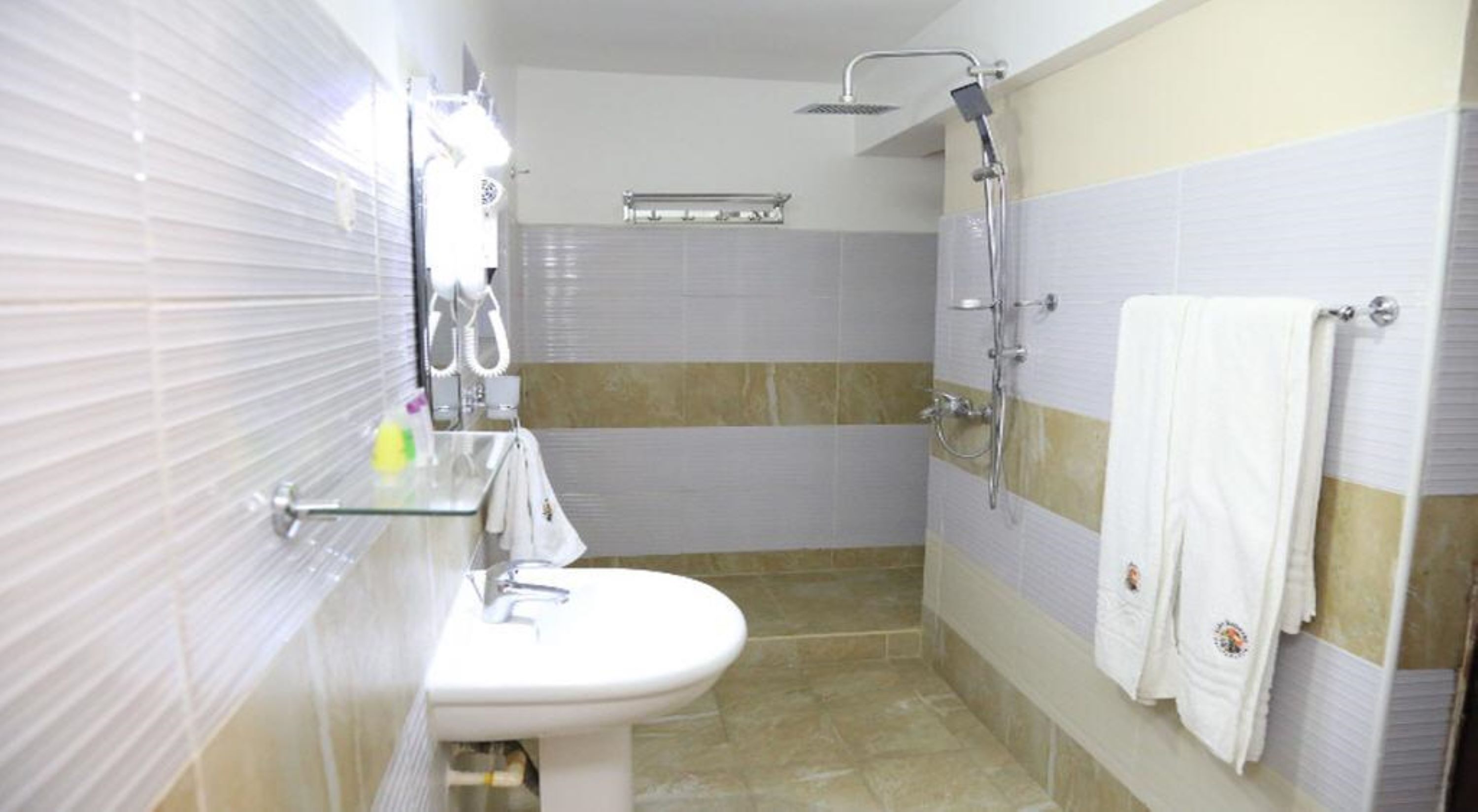 Un baño con lavamanos, espejo, toallero, ducha y paredes de azulejos.