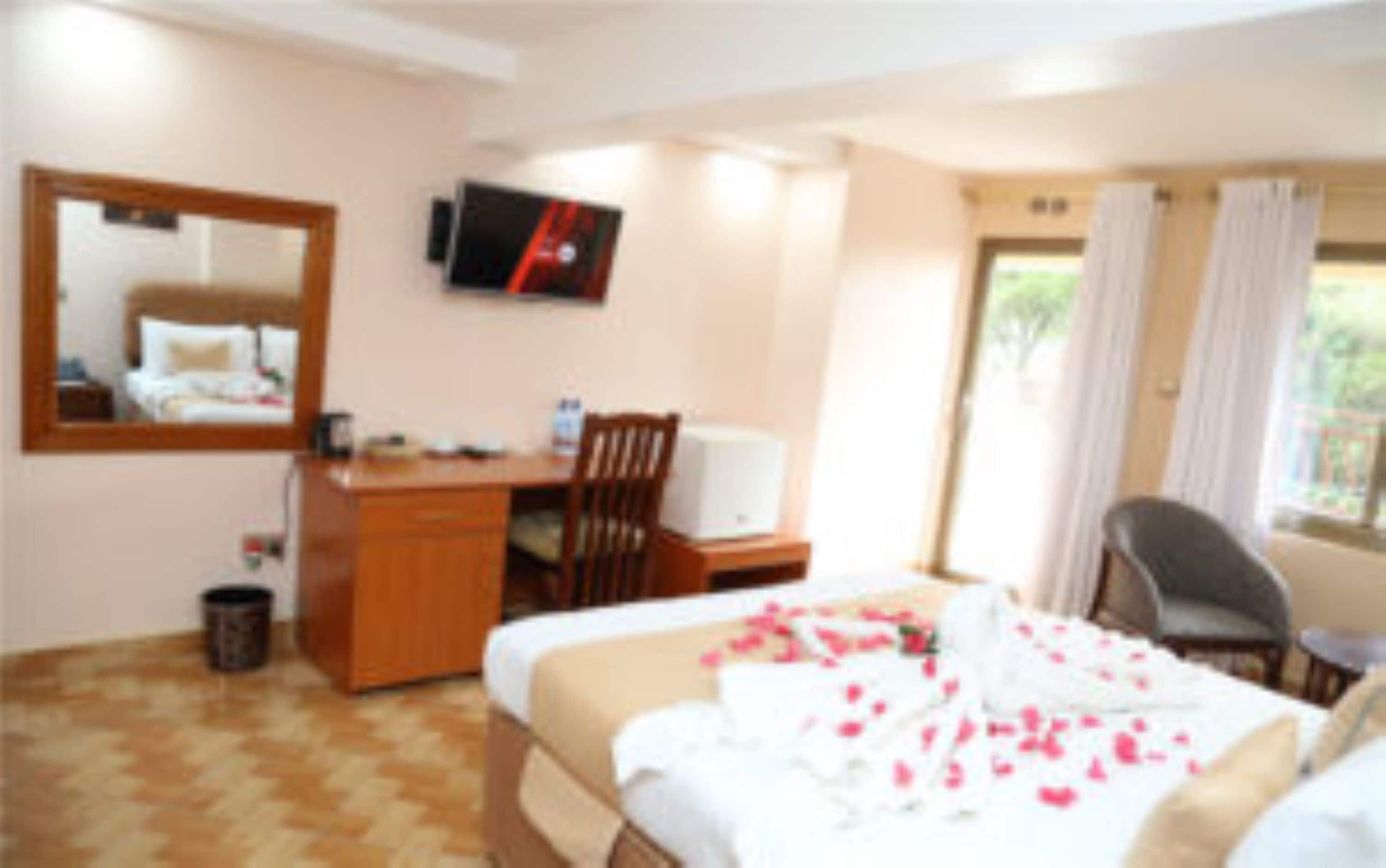 A hotel room with a bed, a desk, a chair, a television, and a window with curtains.