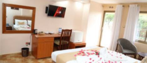 A hotel room with a bed, a desk, a chair, a television, and a window with curtains.