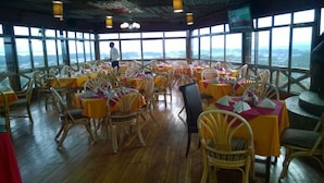 A restaurant with multiple tables and chairs, large windows offering a view of the landscape, and a wooden floor. - Panorama Park Hotel (Naivasha)