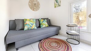 Un salon moderne avec un canapĂ© gris, des coussins colorĂ©s, une horloge murale ronde et une petite table dâappoint.