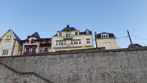 Une rangĂ©e dâimmeubles Ă plusieurs Ă©tages dotĂ©s de balcons, un mur de pierre au premier plan et un ciel dĂ©gagĂ©.