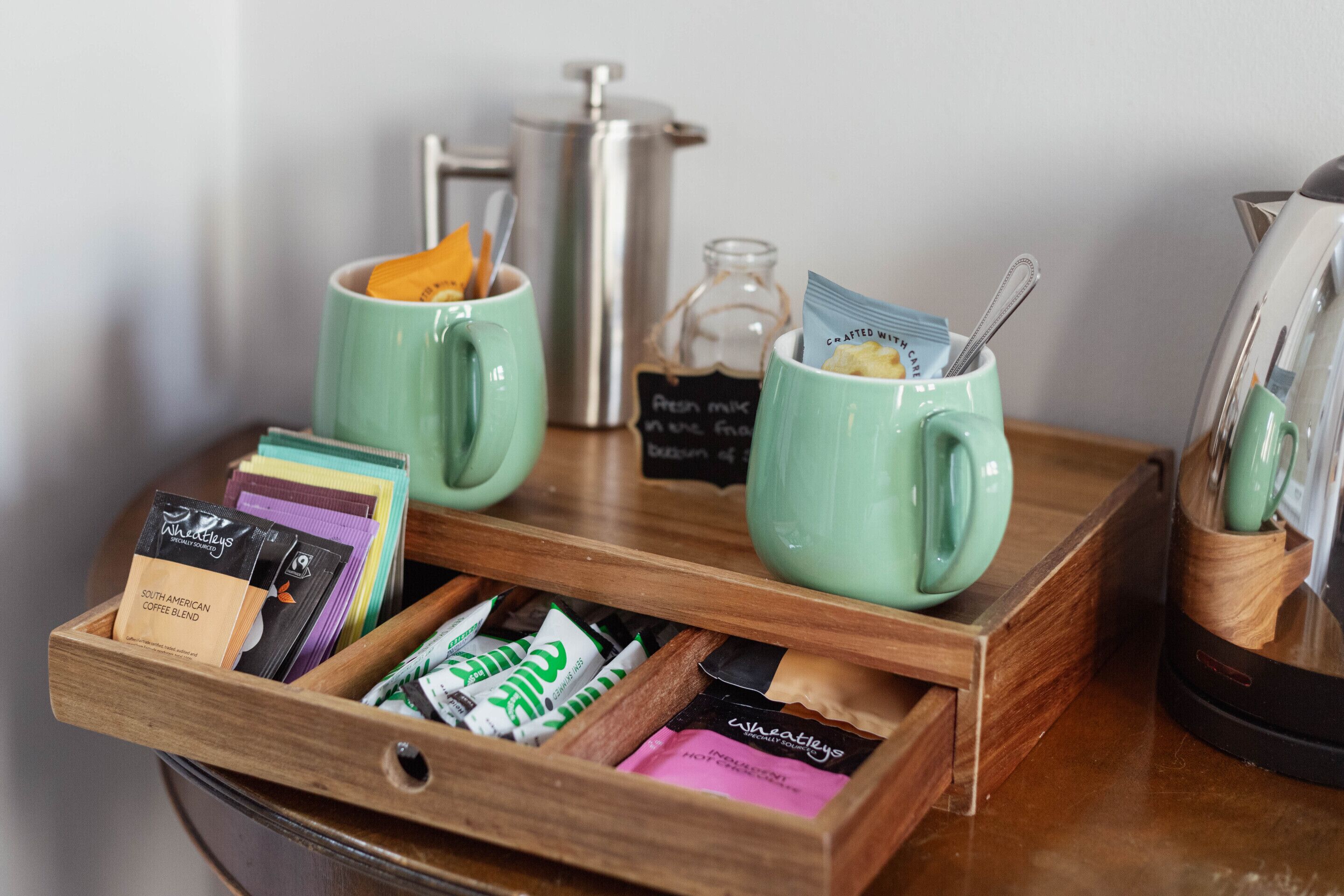 Una estación de café con dos tazas verdes, un molinillo de café y una bandeja con sobres de café.