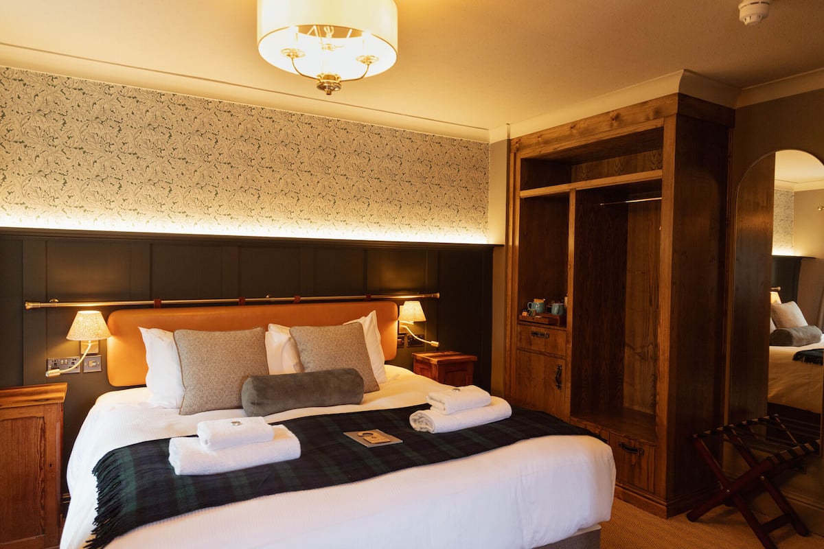 Quarto de hotel com uma cama grande, cabeceira de madeira, um guarda-roupa e um espelho.