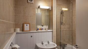 A bathroom with a sink, mirror, shower, and toilet paper.