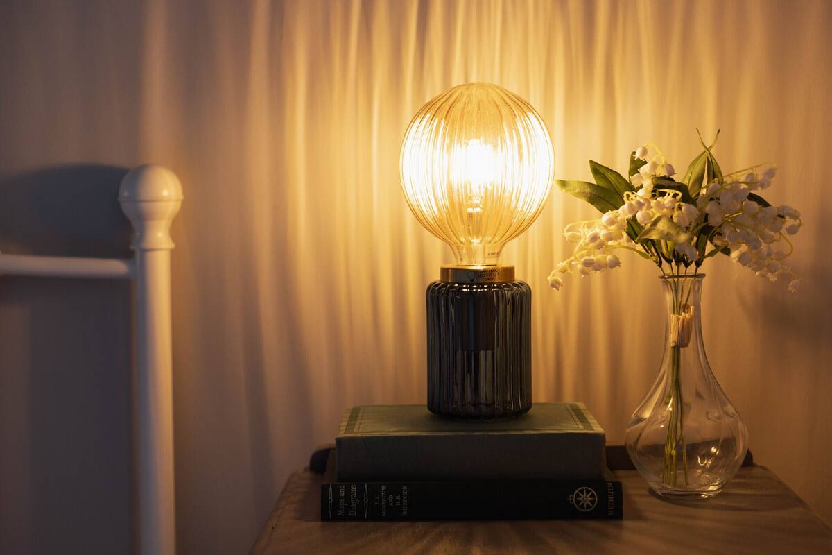 Uma mesa com uma lâmpada, um vaso com flores e livros.