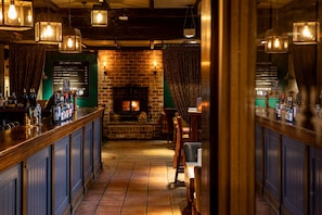 A bar area with a brick fireplace, wooden bar counter, and hanging light fixtures. - The Devonshire Arms Baslow (Bakewell)
