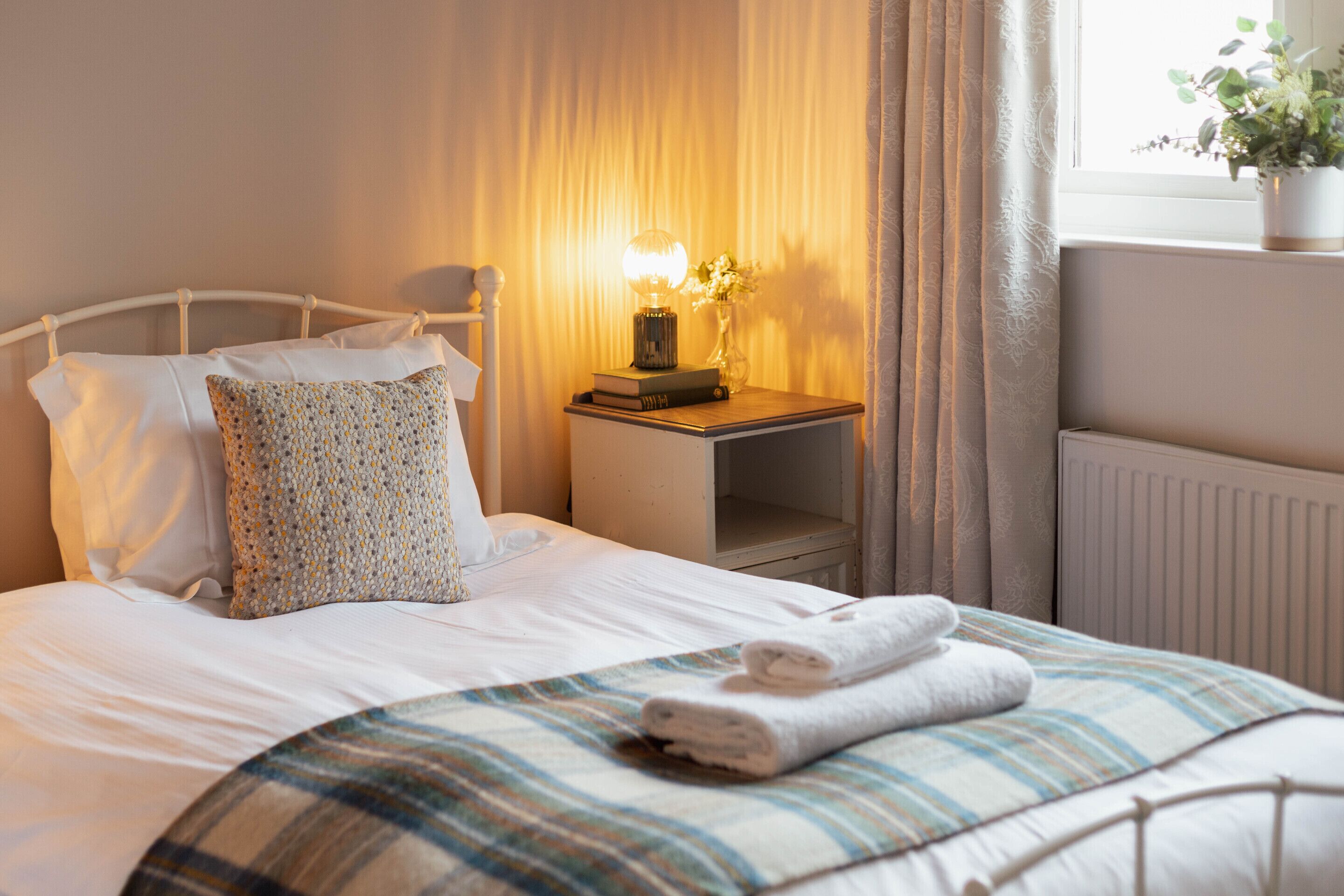 A neatly made bed with a striped blanket, a pillow, and a bedside lamp.