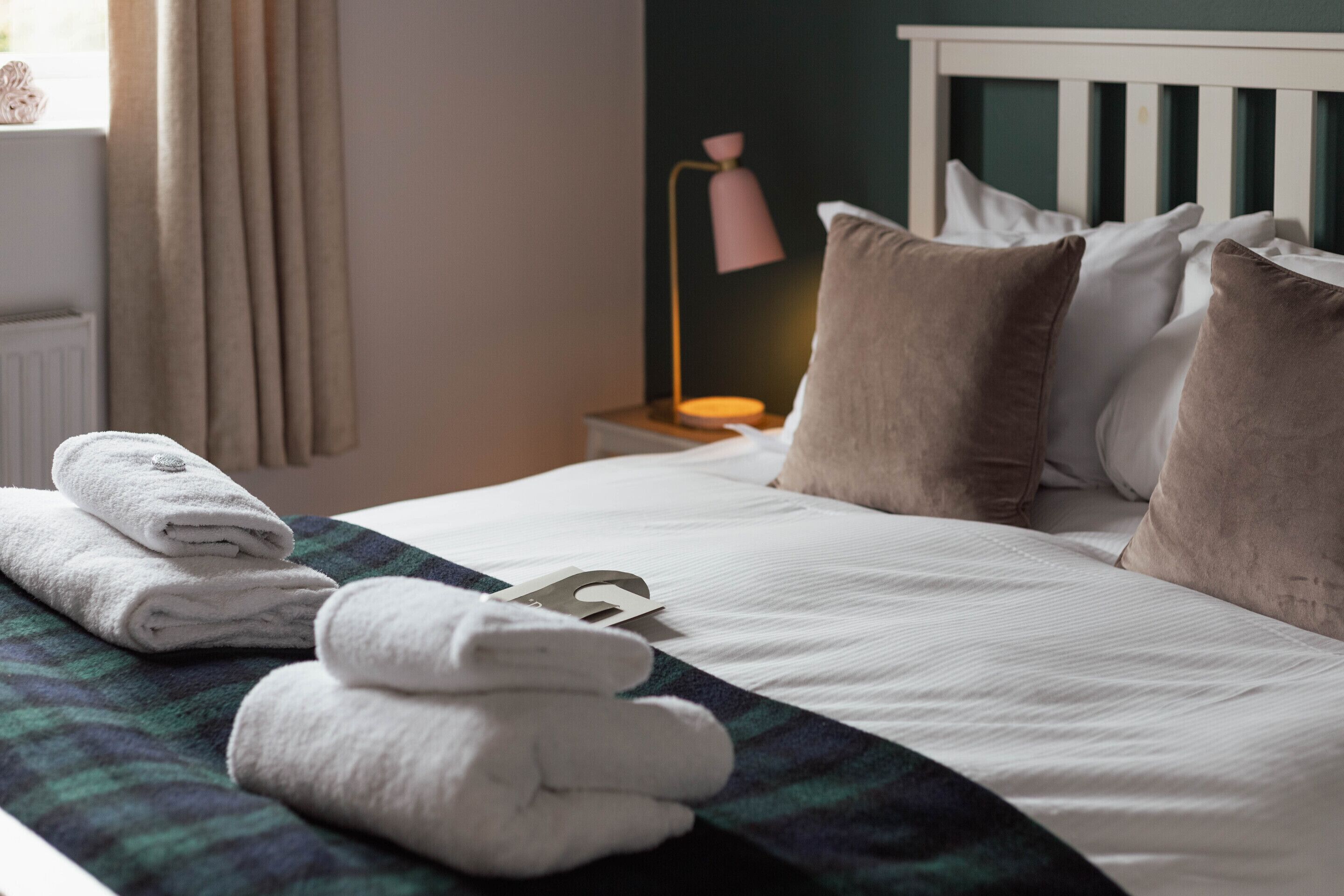 A neatly made bed with white linens and a folded towel on the side.