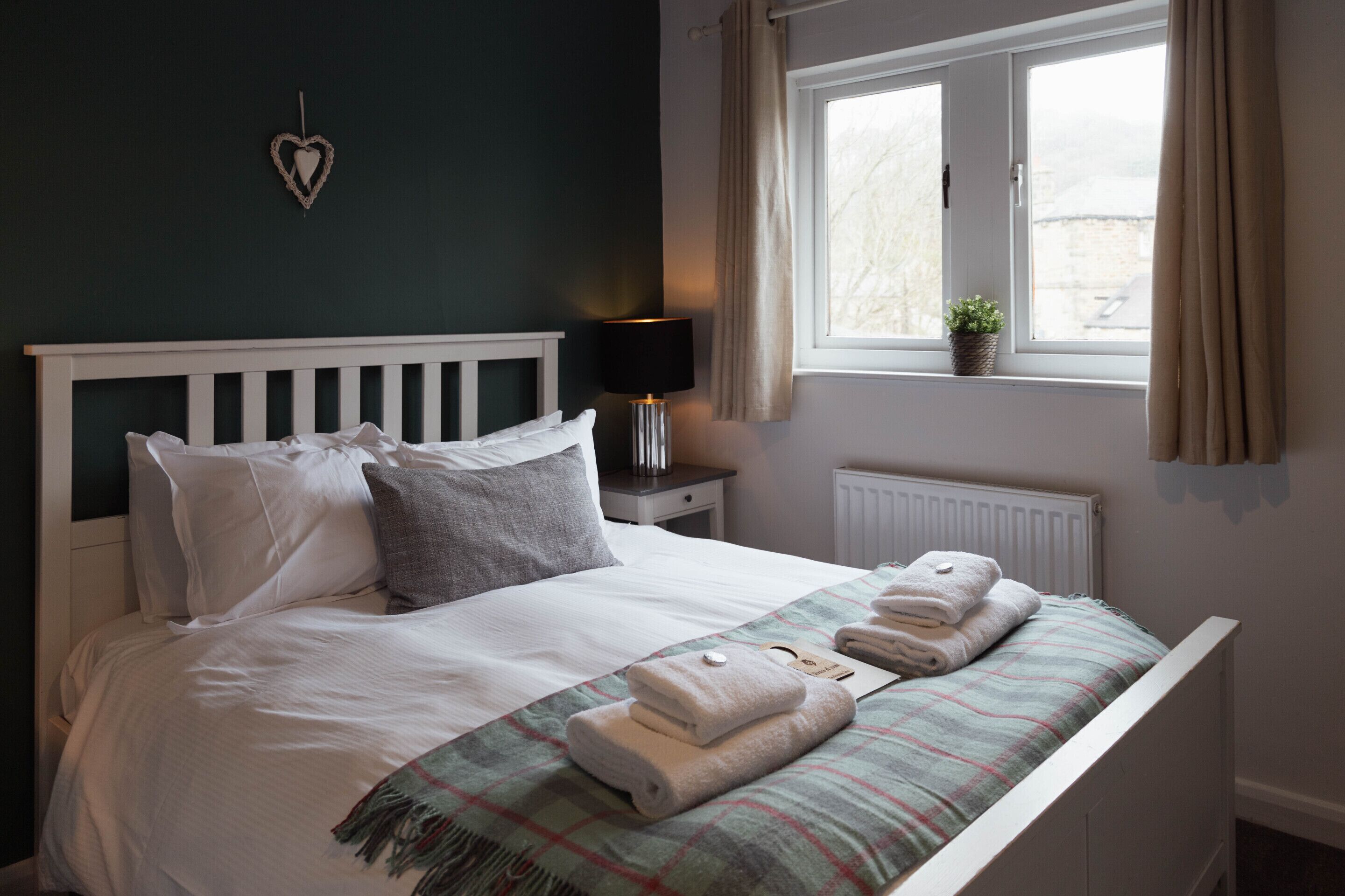 A neatly made bed with pillows, a bedside lamp, and a window with curtains.