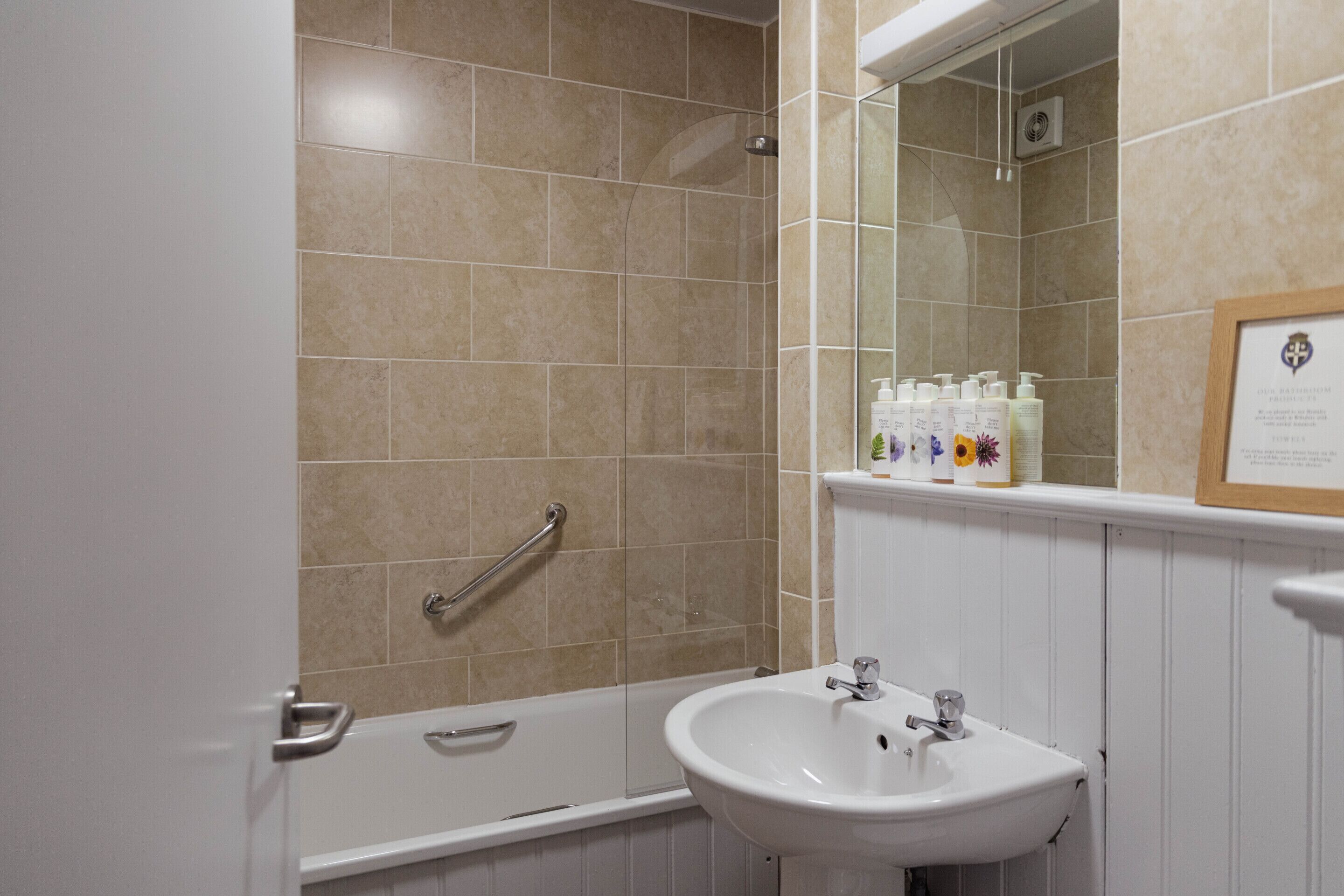 A bathroom with a bathtub, a sink, and a shower. There are toiletries on the shelf above the sink.