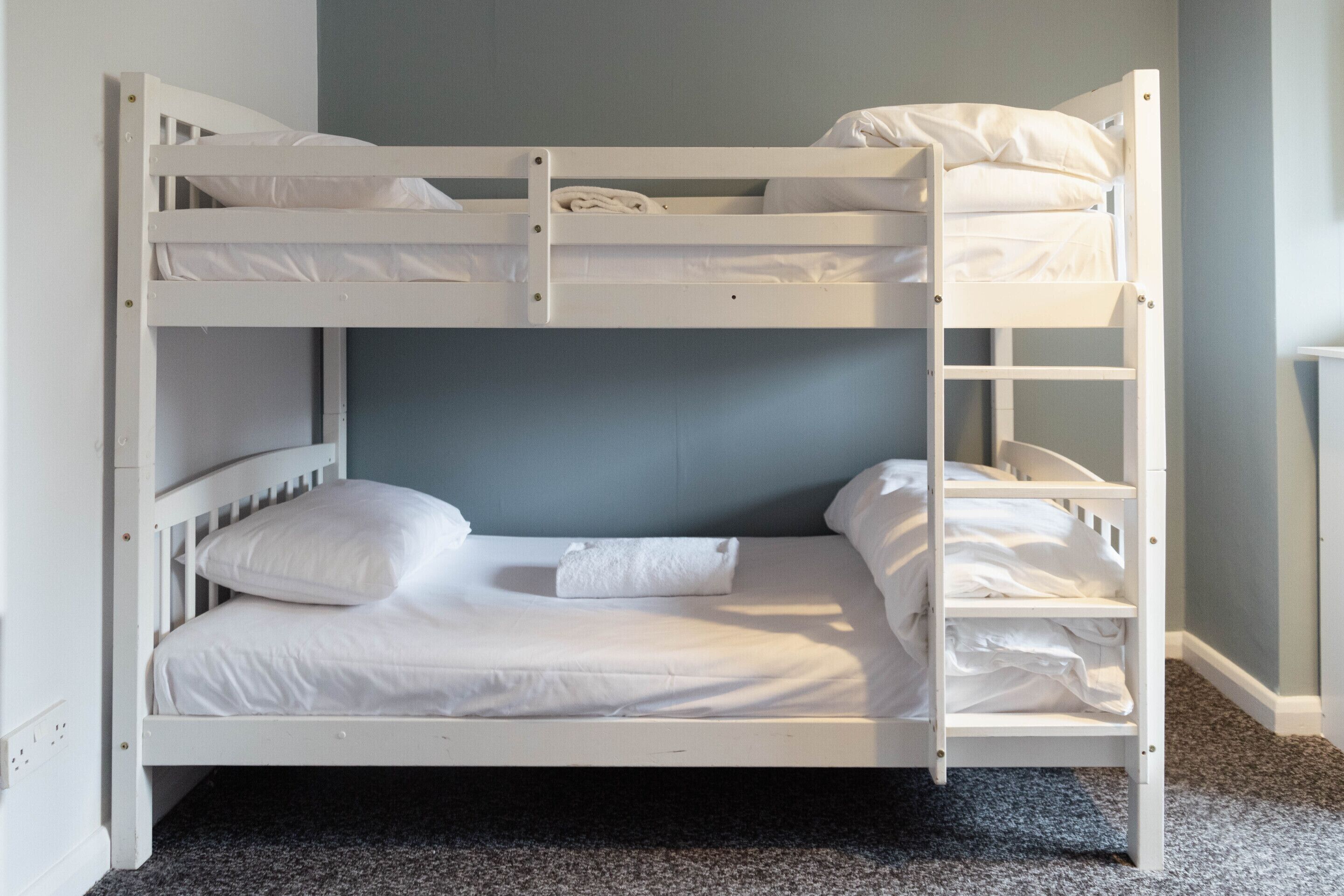 Una cama litera con ropa de cama blanca y pared gris.