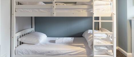 Una cama litera con ropa de cama blanca y pared gris.