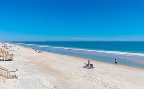 A beach with a wooden walkway leading to the water, a pier in the distance, and people relaxing on the sand. - Topsail State of Mind - 4BR Oceanfront Home; Elevator; Covered Porch (Surf City)