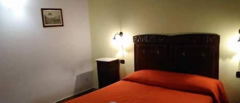 A hotel room with a bed, two bedside tables, a nightstand, and wall-mounted lamps.