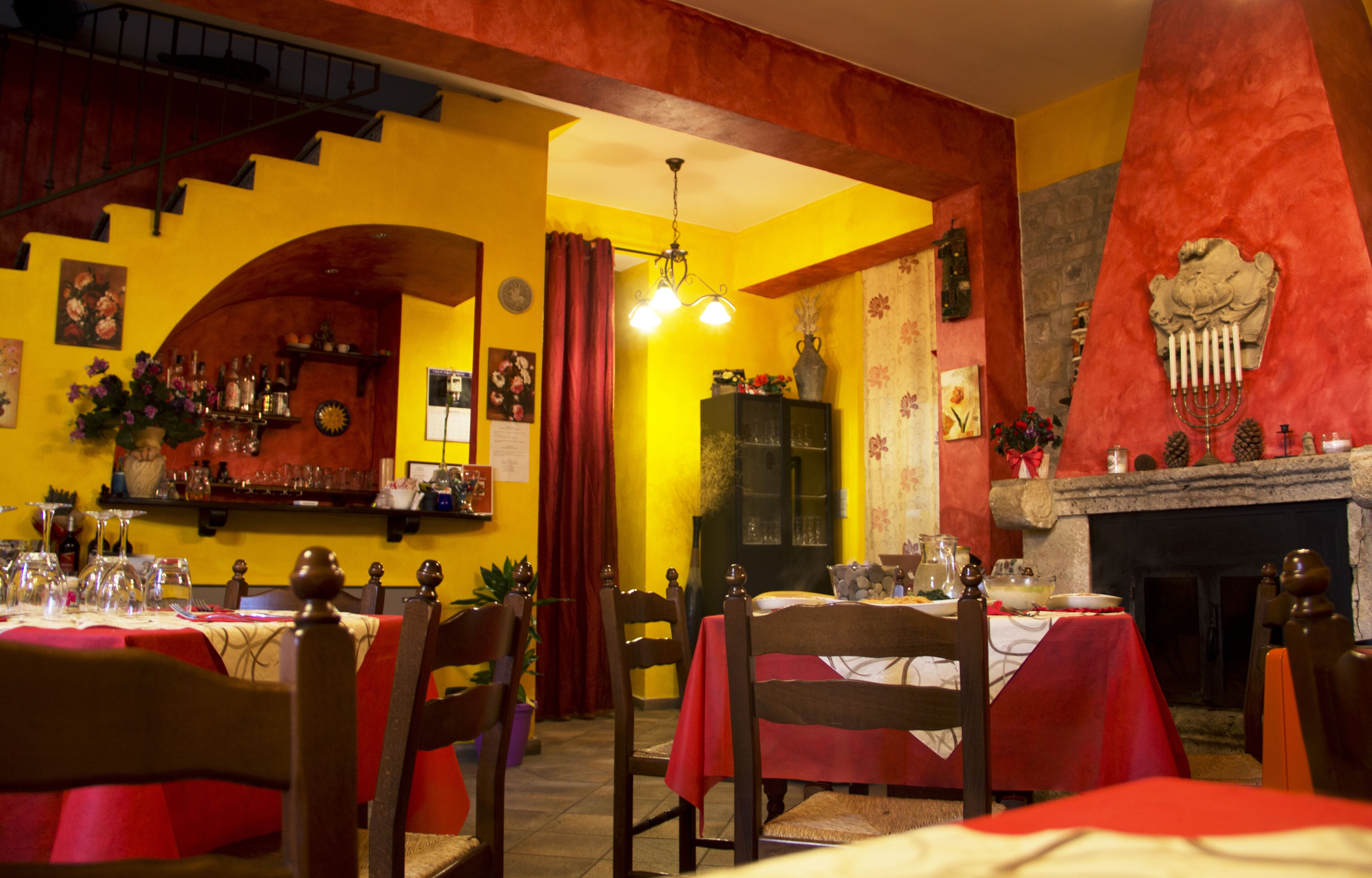 Un comedor con mesas dispuestas para una comida, sillas, una zona de bar con botellas y una chimenea.