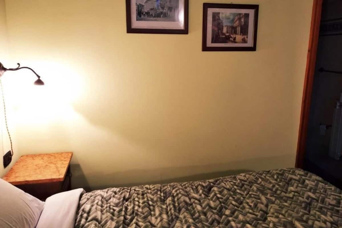 A room with a bed, a nightstand, and two framed pictures on the wall.