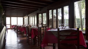 A restaurant with multiple tables covered with red tablecloths, wooden chairs, and large windows offering a view of the outdoors. - I Templari (Polizzi Generosa)