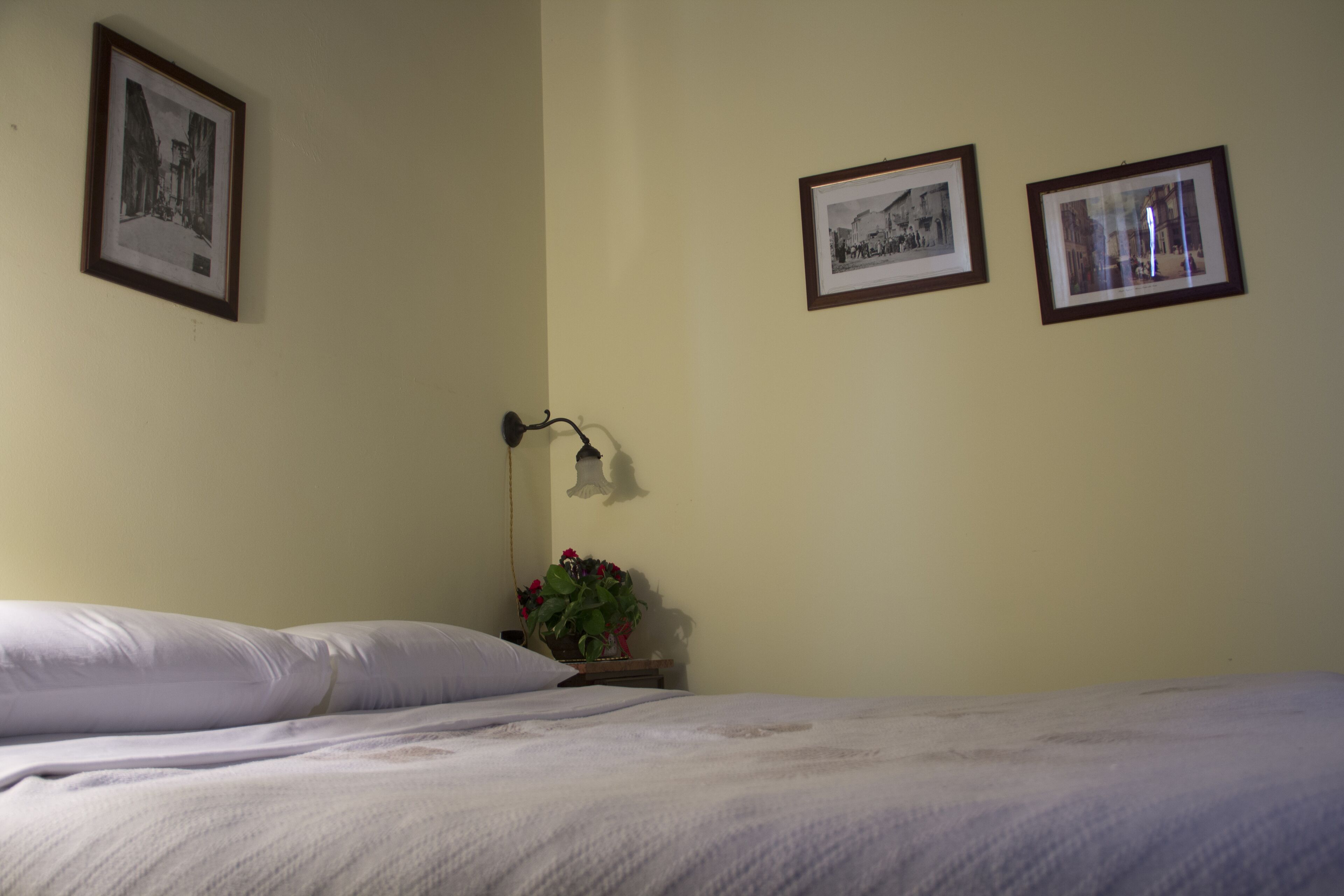 Ein Schlafzimmer mit einem Bett, Kissen, einem Nachttisch mit Lampe und zwei gerahmten Bildern an der Wand.