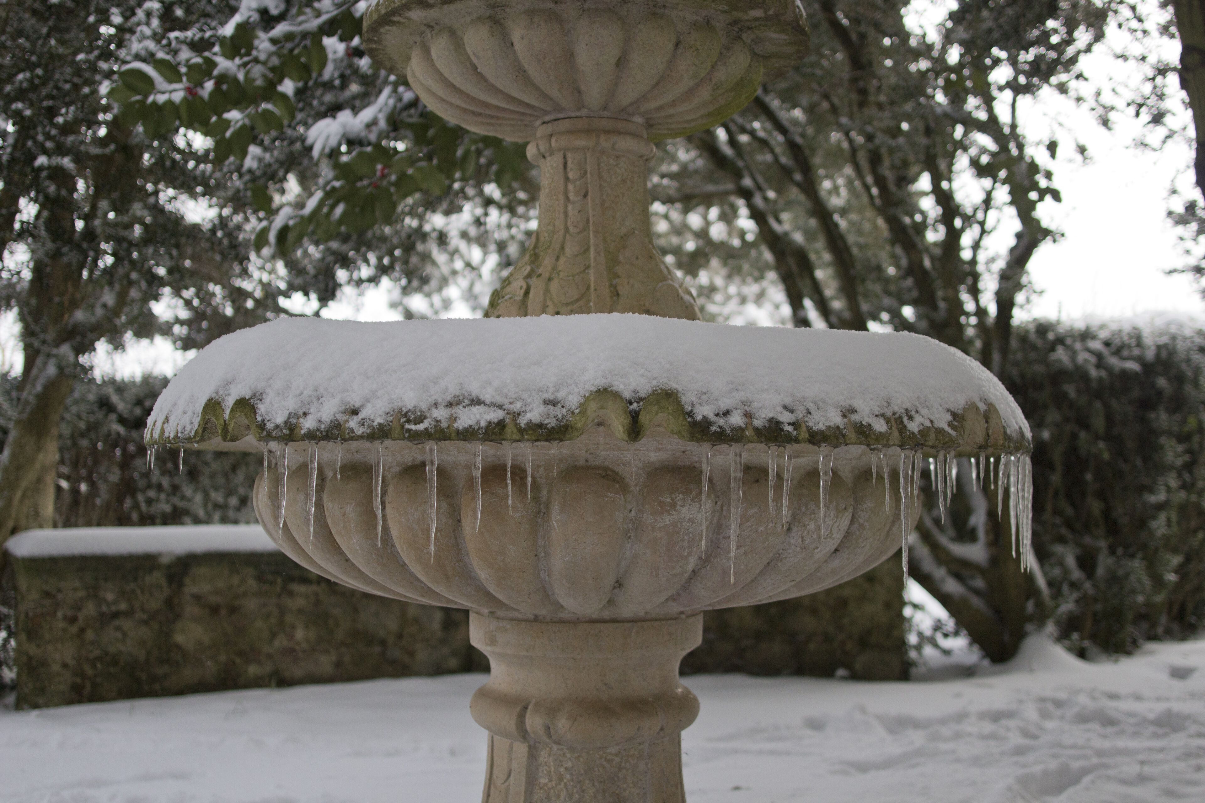 Une fontaine en pierre recouverte de neige et ornée de glaçons.