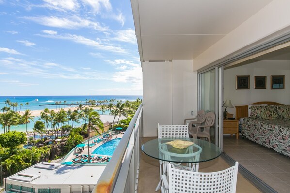 Relax on the balcony overlooking the resort pool, surrounded by palm trees and sun loungers.