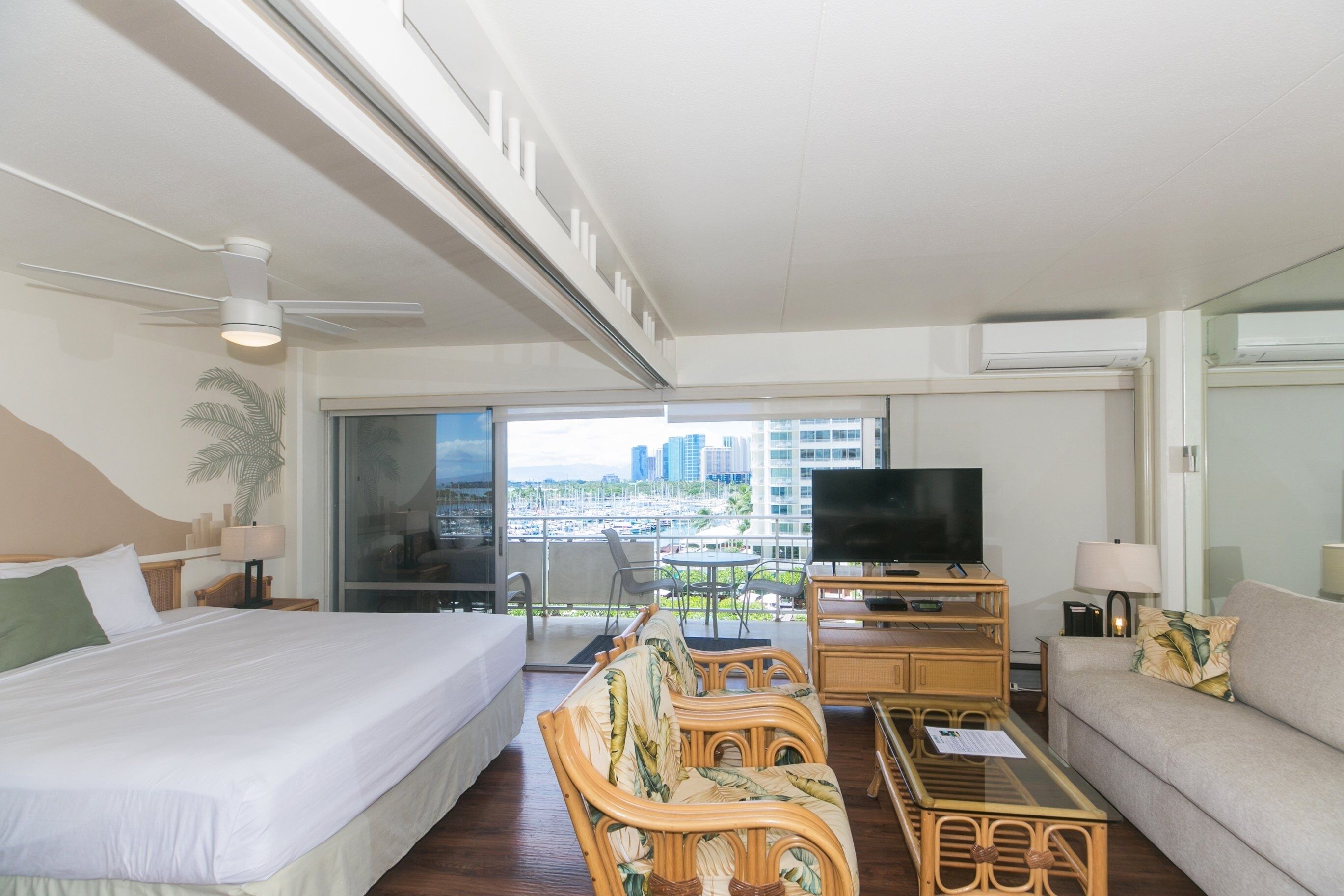 A hotel room with a bed, a sofa, a television, and a balcony with a city view.
