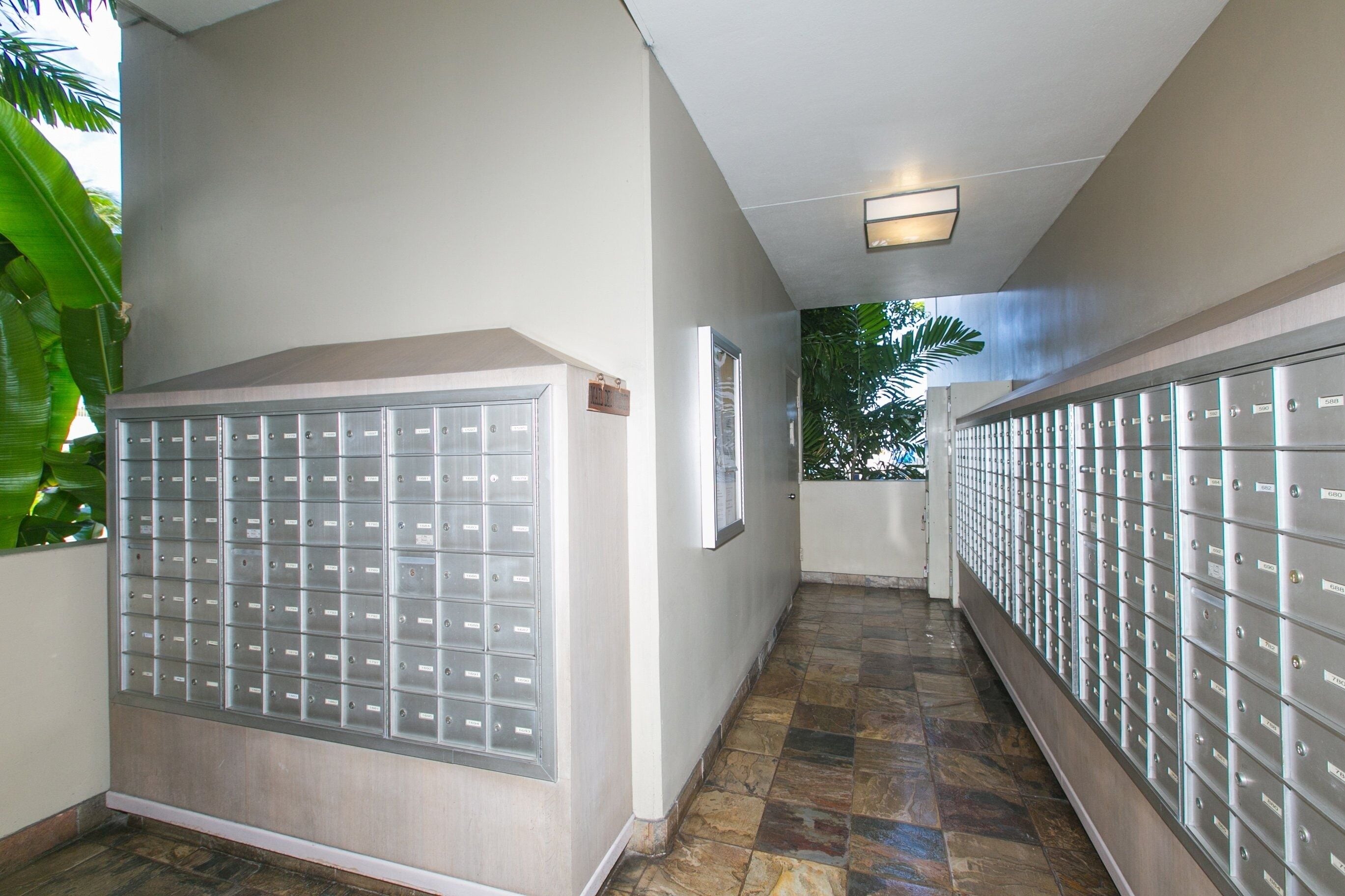 A hallway with a row of metal lockers on both sides, a tiled floor, and a ceiling light fixture.