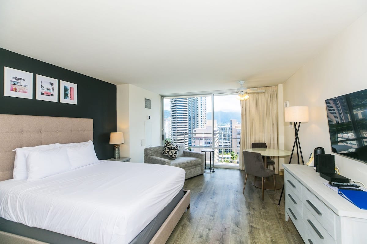 A hotel room with a large bed, a desk, a chair, a small table, and a TV.