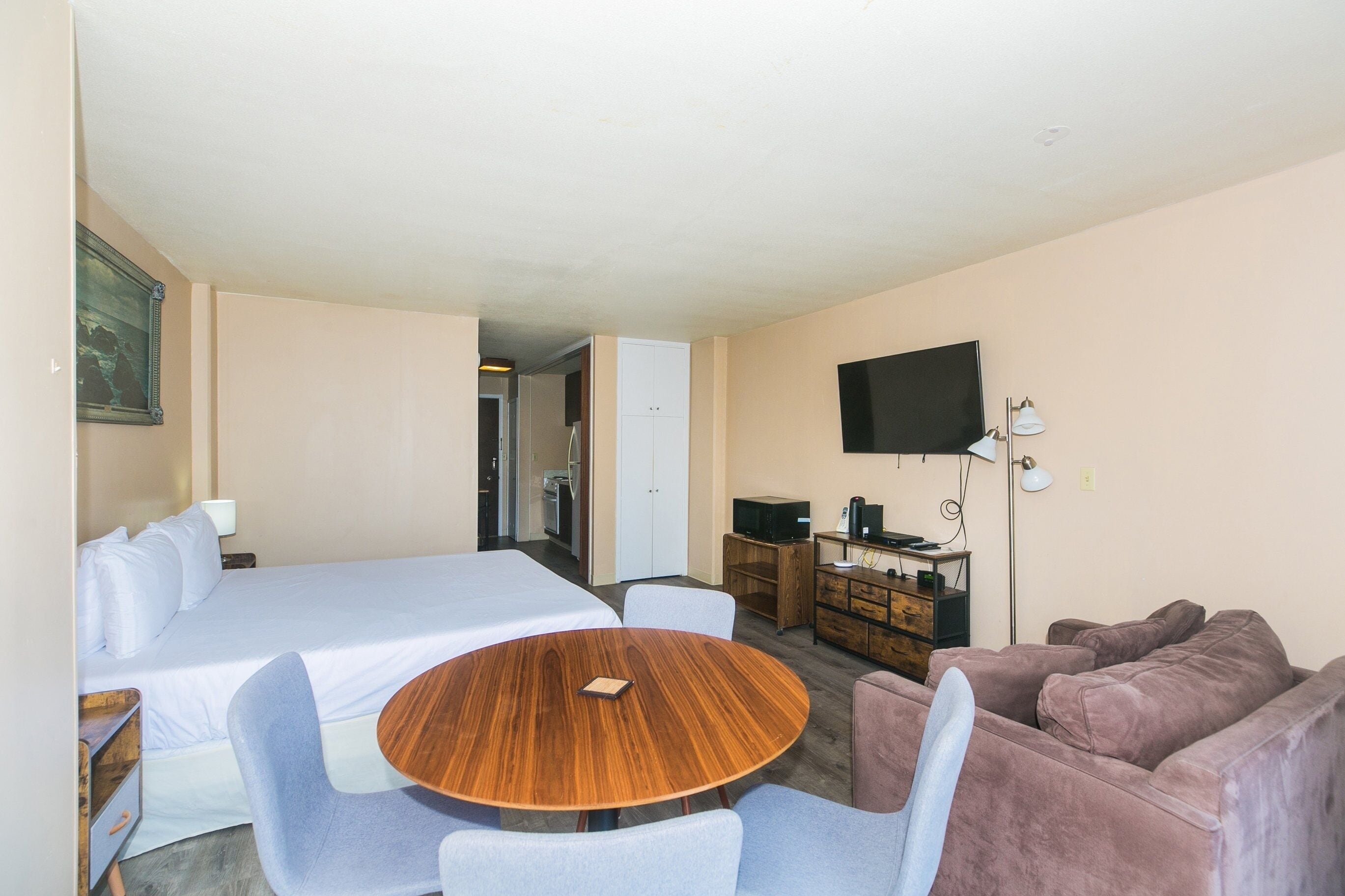 A room with a bed, a round table with chairs, a sofa, a TV, and a desk with a lamp.