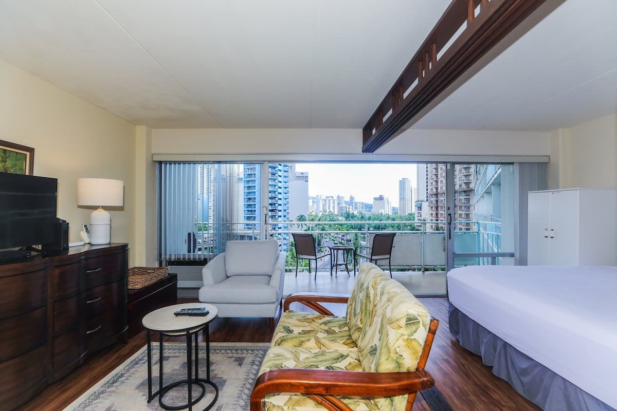 Una habitación de hotel moderna con balcón, cama, sofá, televisor y escritorio.