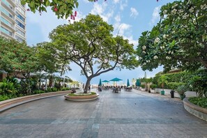 A spacious outdoor area with a large tree, outdoor seating, and a view of a building in the background.