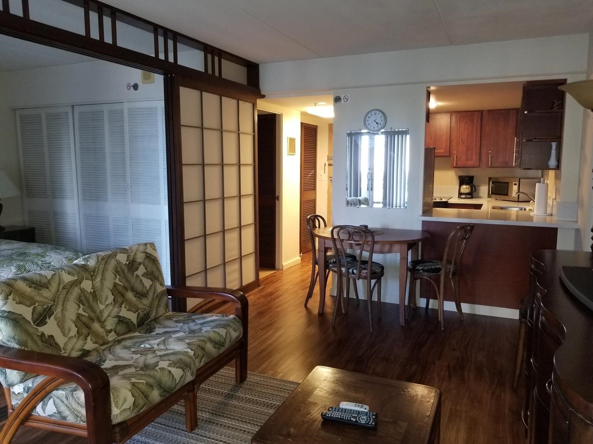 A room with a bed, a sofa, a dining table with chairs, a kitchen area with cabinets and appliances, and a sliding door with a grid pattern.