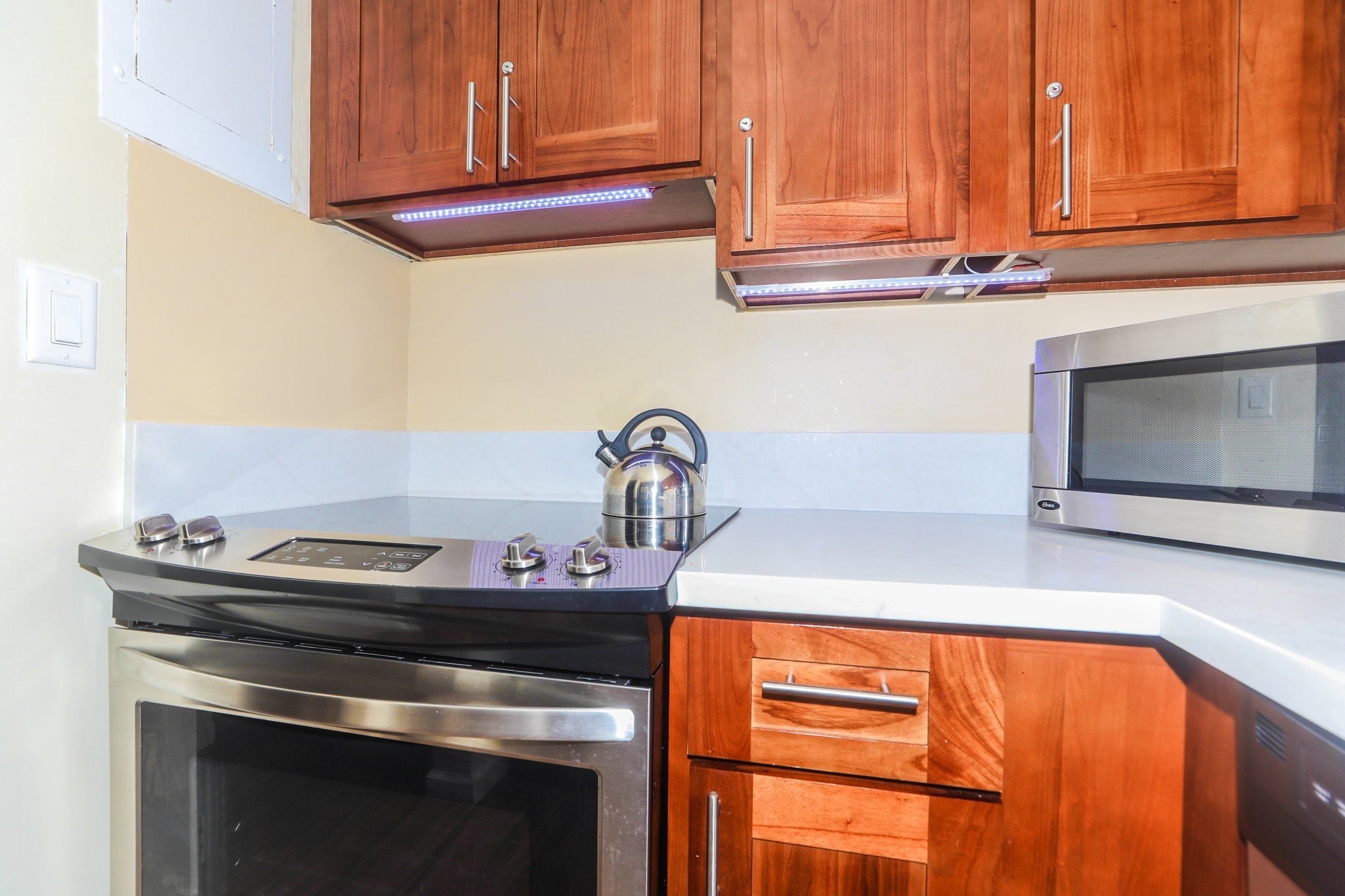 A kitchen with wooden cabinets, a stainless steel stove, a kettle, and a microwave.