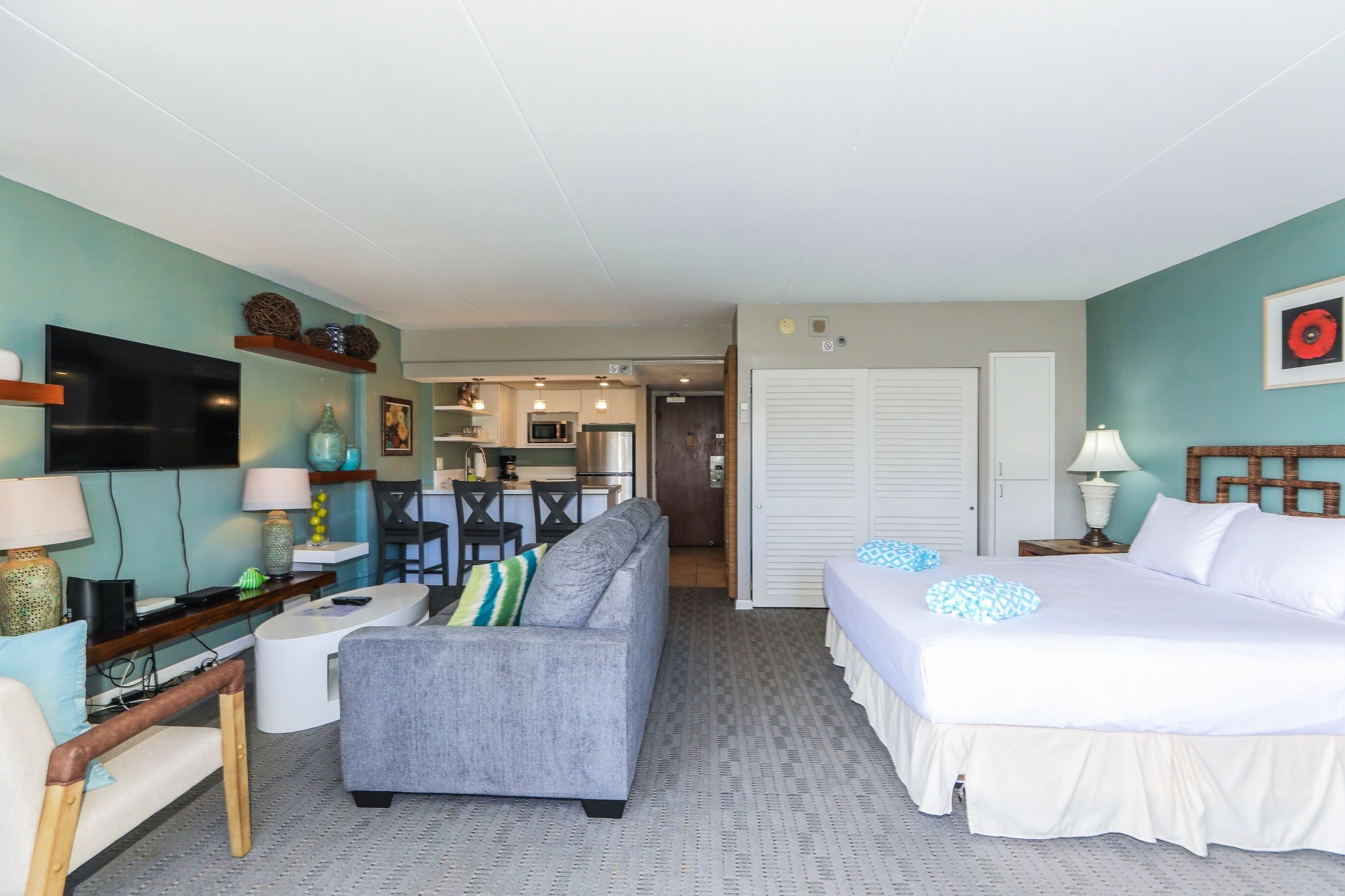 A hotel room with a sofa, a bed, a TV, a desk, and a kitchenette.