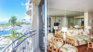 A balcony with a view of a marina and cityscape, furnished with wicker chairs and a sofa, and a glass door leading to the interior. - Ilikai Marina One Bedroom Harbor View Condos - Walk to Ala Moana Beach Park! (Honolulu)